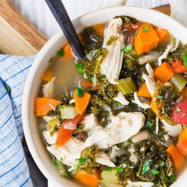 Colorful bowl of soup with chicken, kale, carrots.