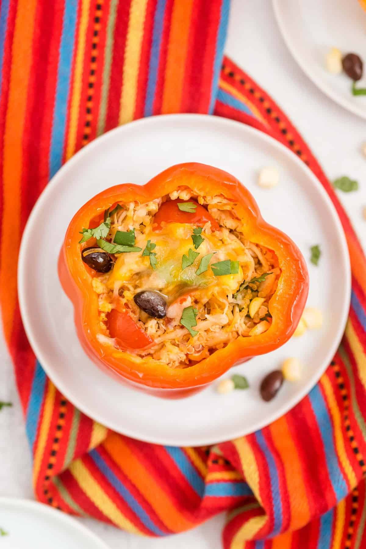 A stuffed pepper on a white plate on top of a colorful linen.
