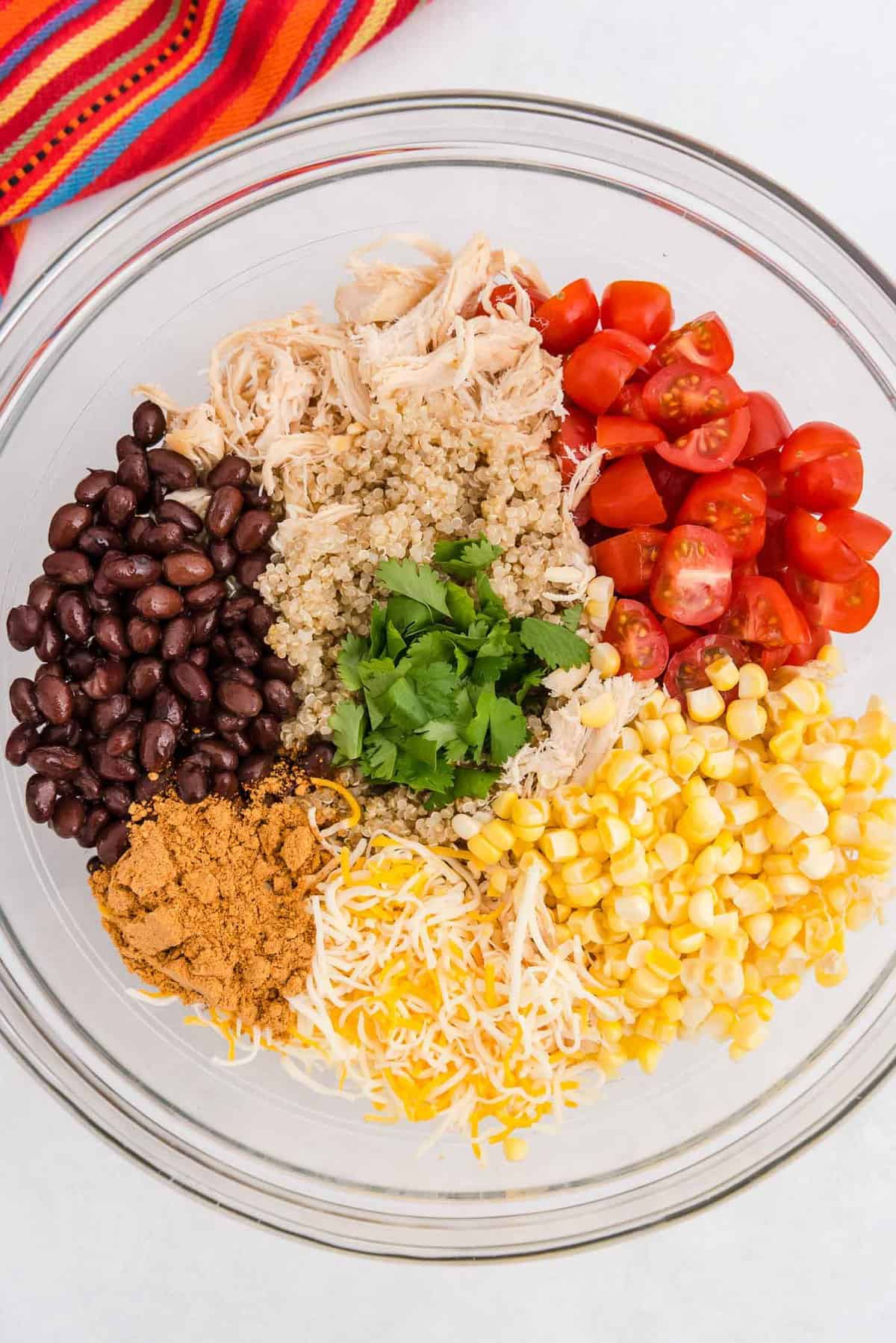 Colorful ingredients in a glass bowl: quinoa, chicken, black beans, tomatoes, and more.