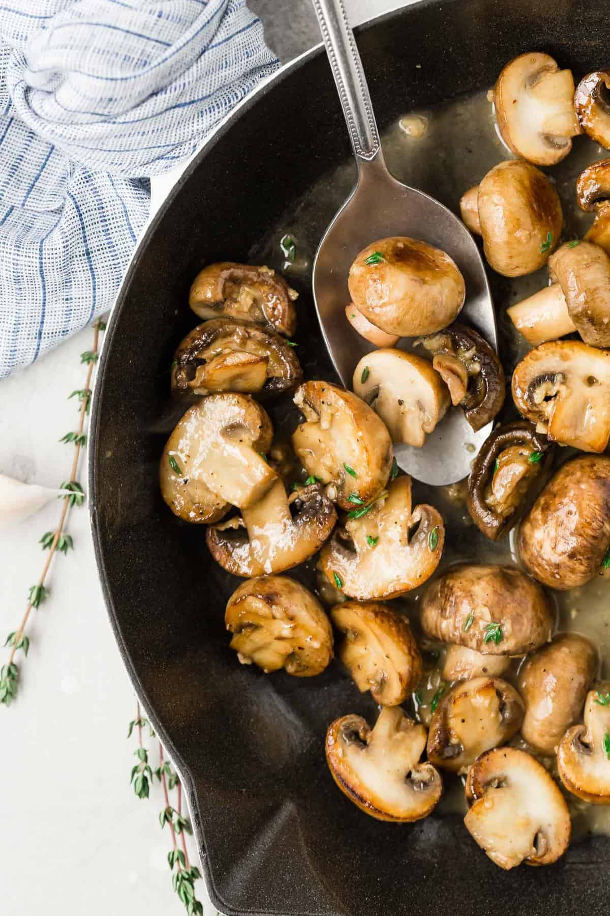 Cooked mushrooms in a butter sauce in a black pan.