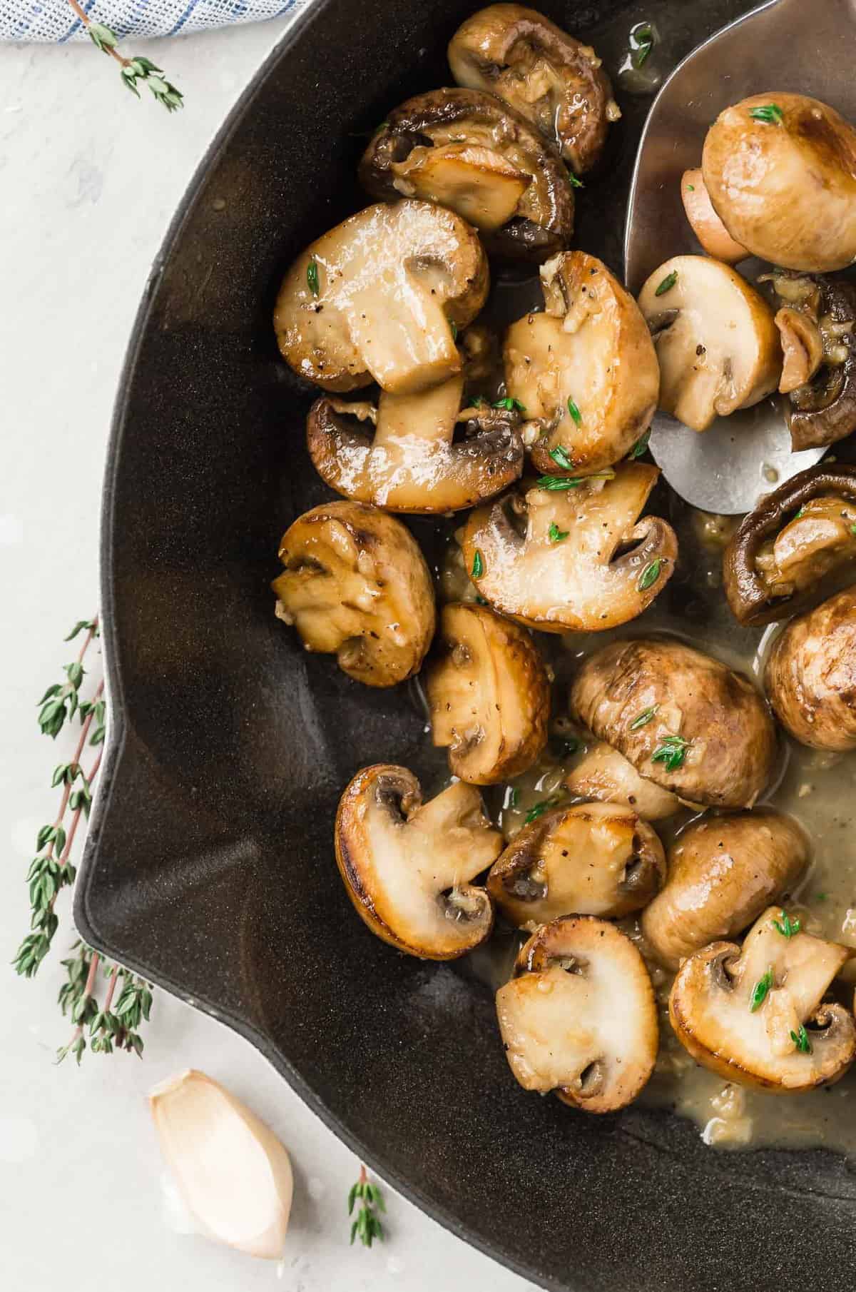 Mushrooms in a white wine sauce in a pan, with fresh thyme.