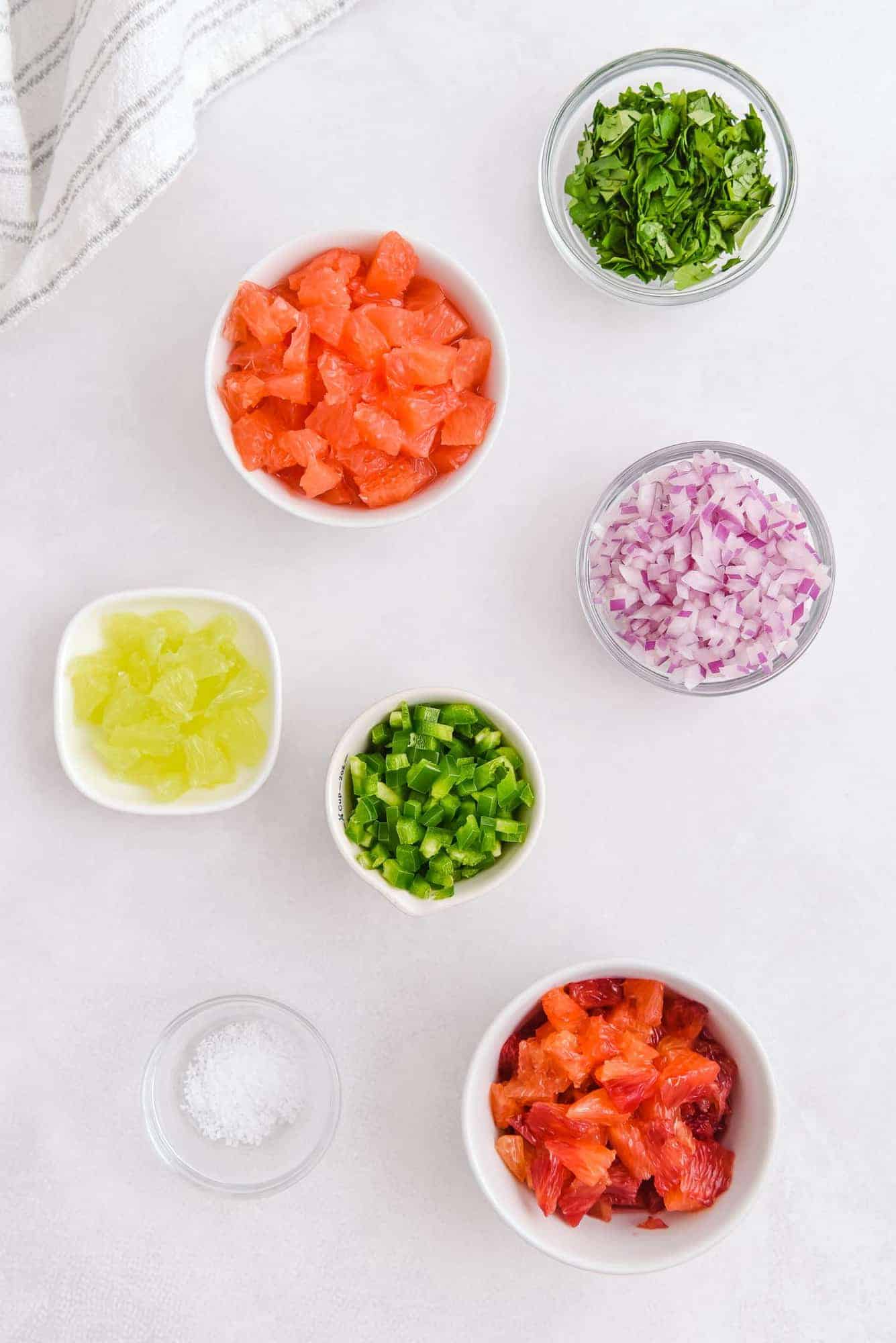 Overhead view of small bowls of ingredients including onions, jalapeno, grapefruit, oranges, cilantro, and lime.