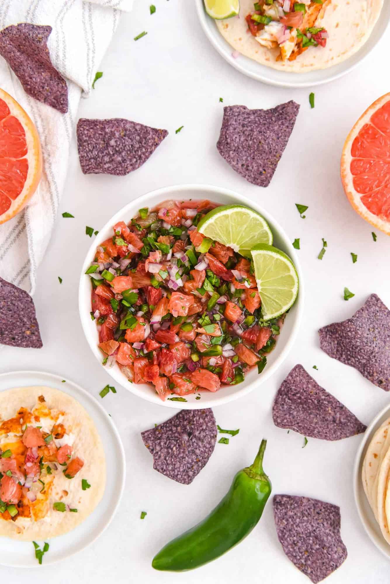 Bowl of citrus salsa surrounded by chips and whole ingredients.