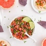 Colorful salsa with oranges and grapefruit in a bowl with a spoon and lime wedges.