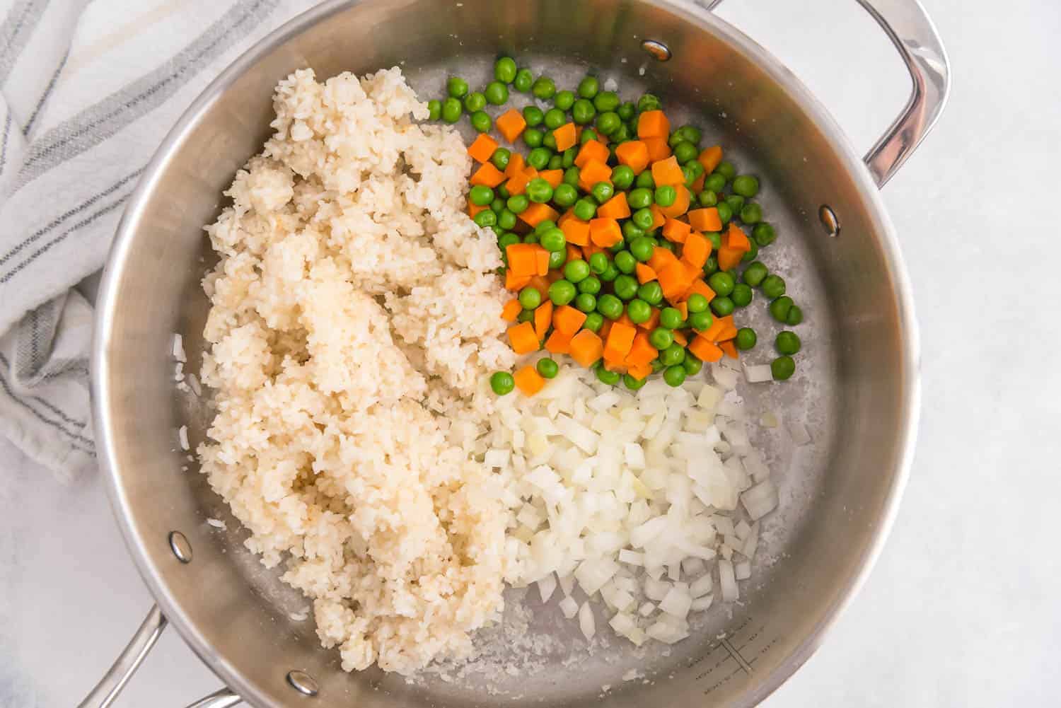 Rice on one side of a pan, green peas, carrots, and onions on the other side.