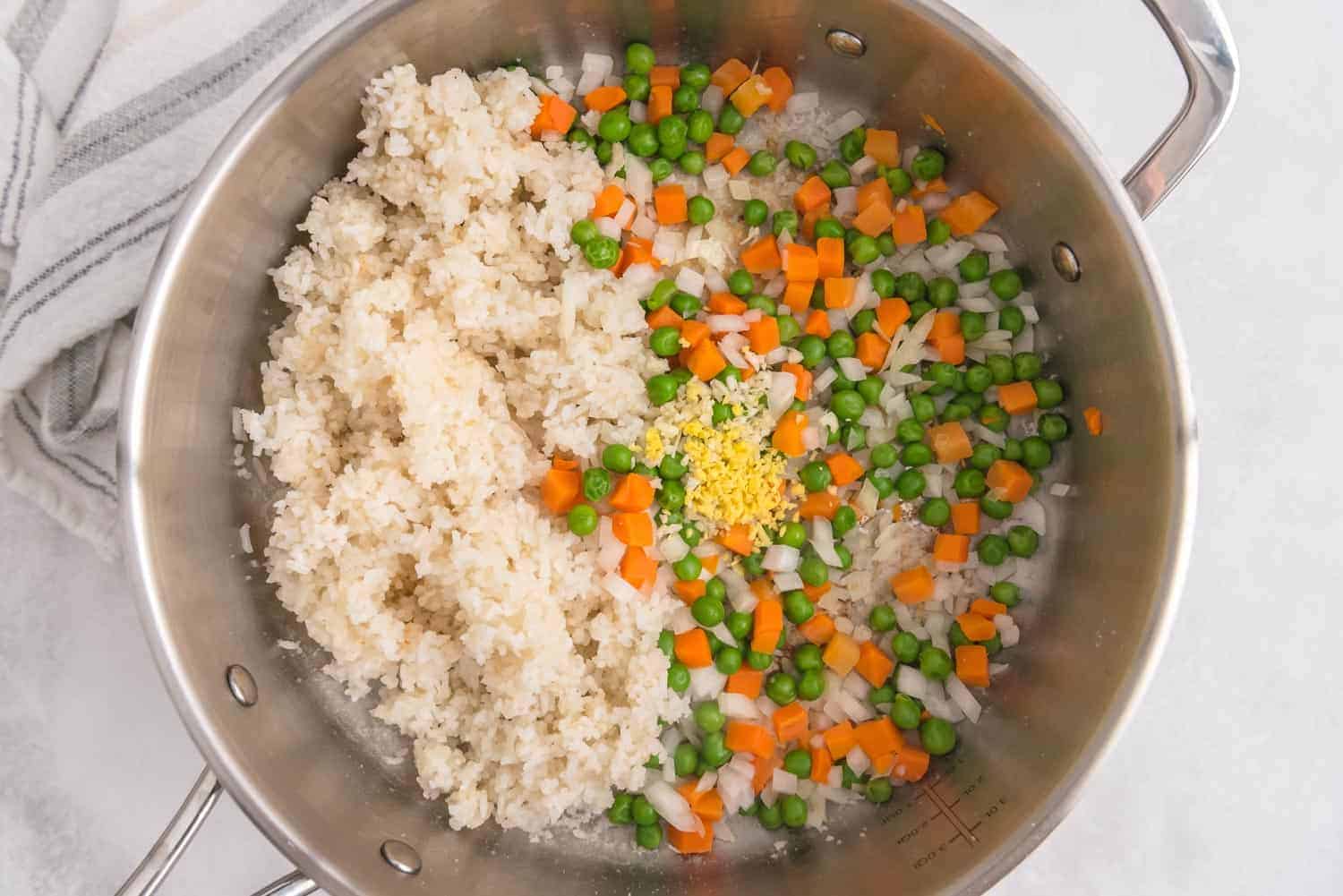 Ginger and garlic on top of vegetables and rice in a saute pan.