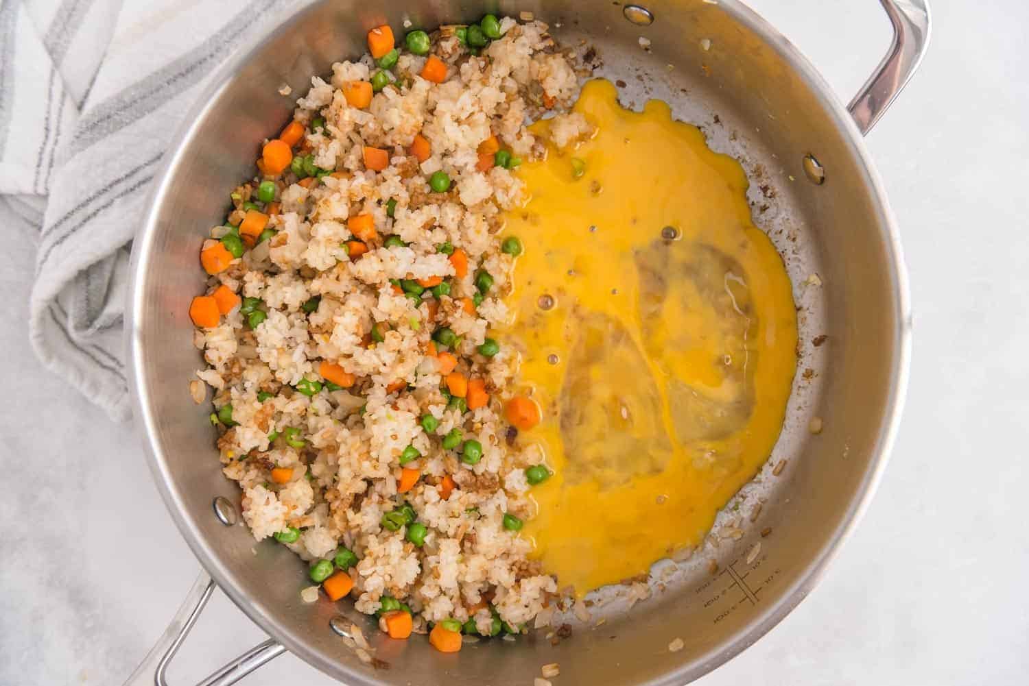 Eggs on one side of a pan, rice and vegetables on the other side.