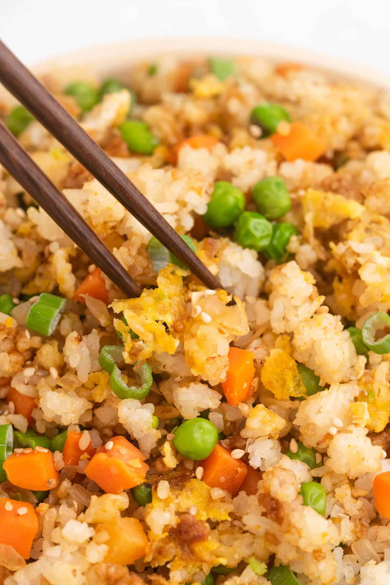 Close up of rice, vegetables, and scrambled eggs between two brown chopsticks.