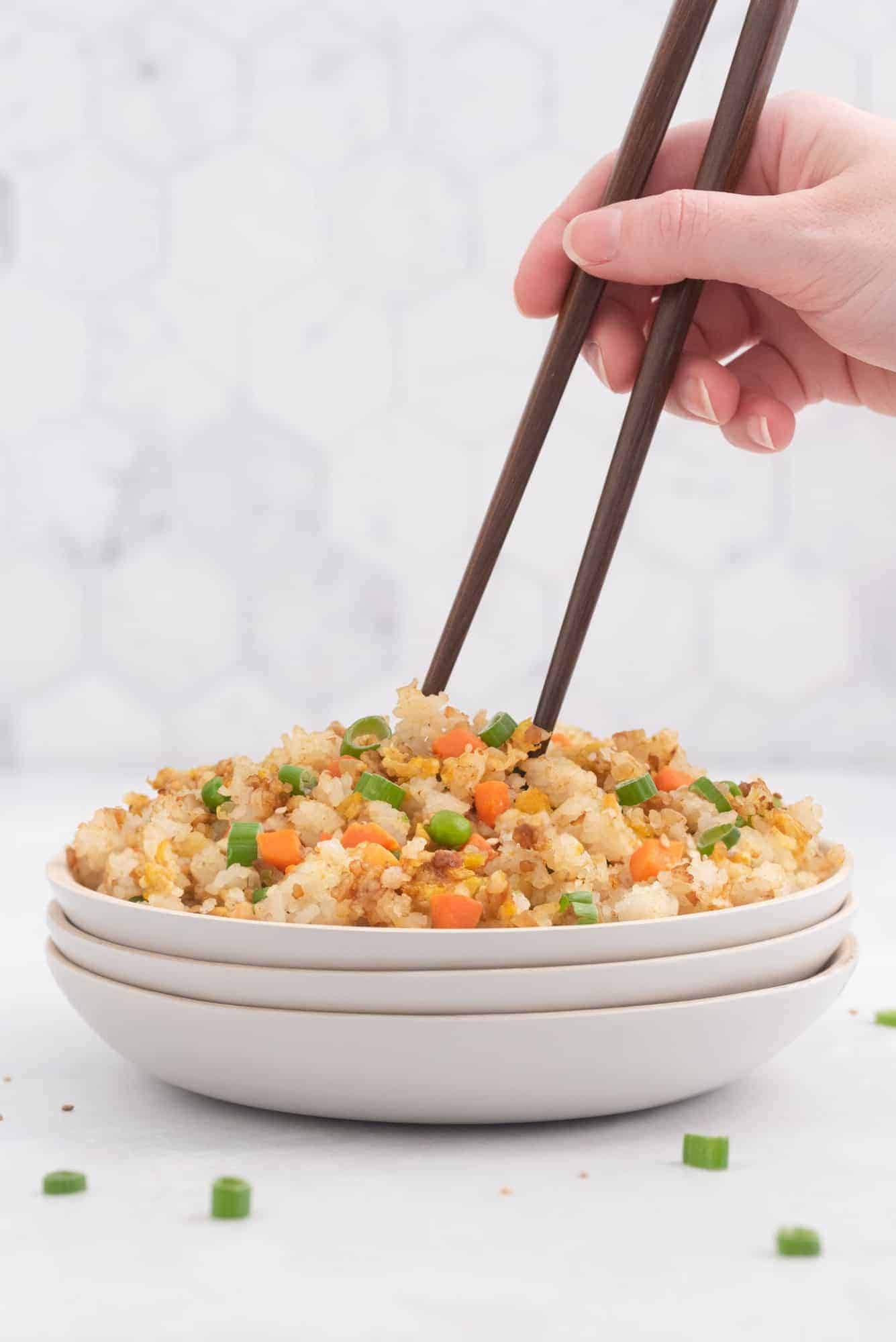 A hand with chopsticks scooping into a bowl of fried rice.