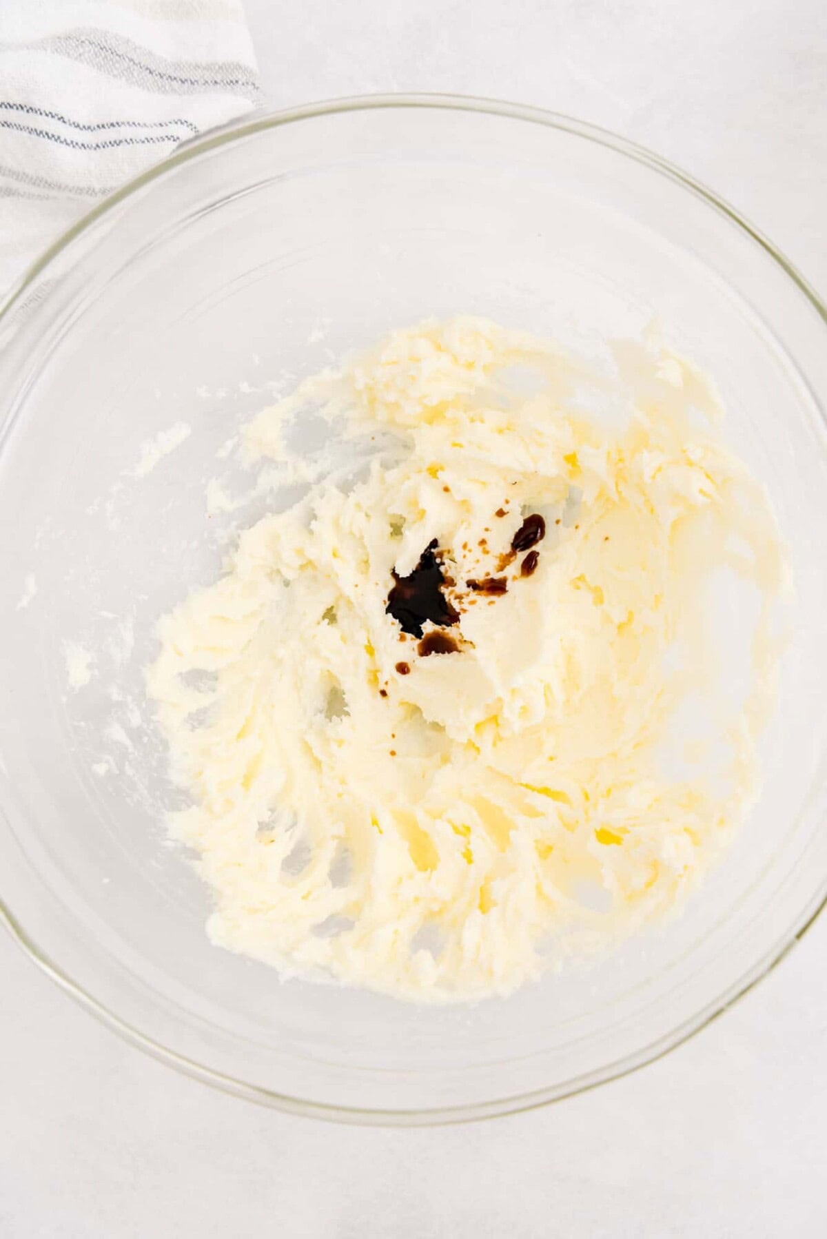 A glass bowl containing creamed butter and sugar with a small amount of vanilla extract added in the center.