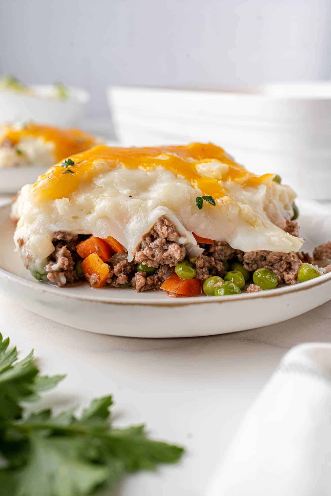 Slice of shepherd's pie on a white plate, parsley in foreground.