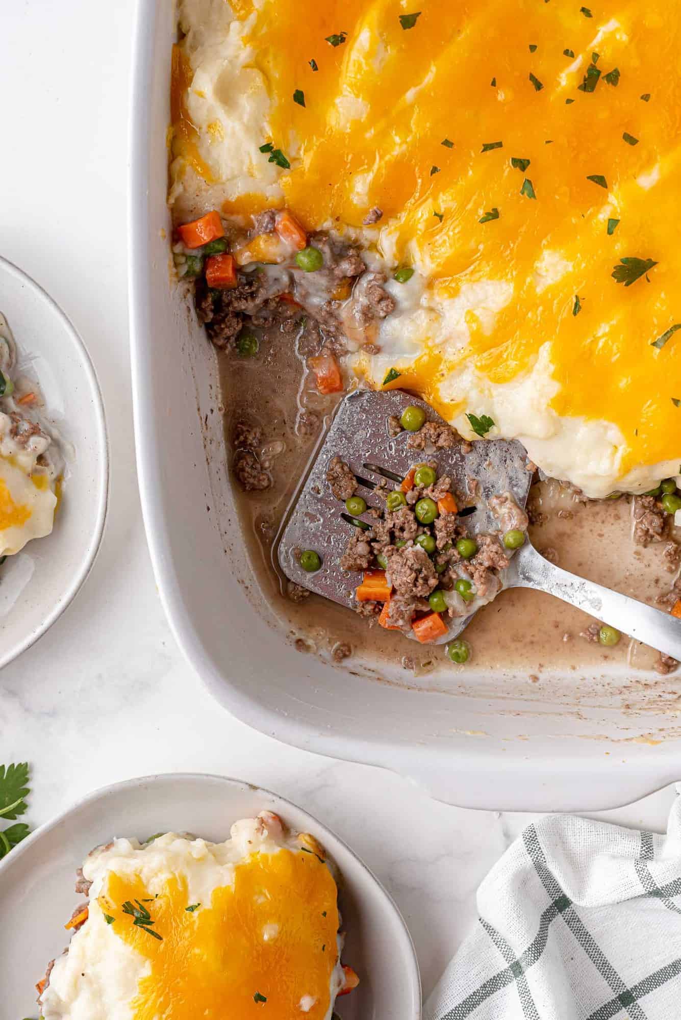 Shepherd pie being scooped out of a white baking dish with a metal spatula.