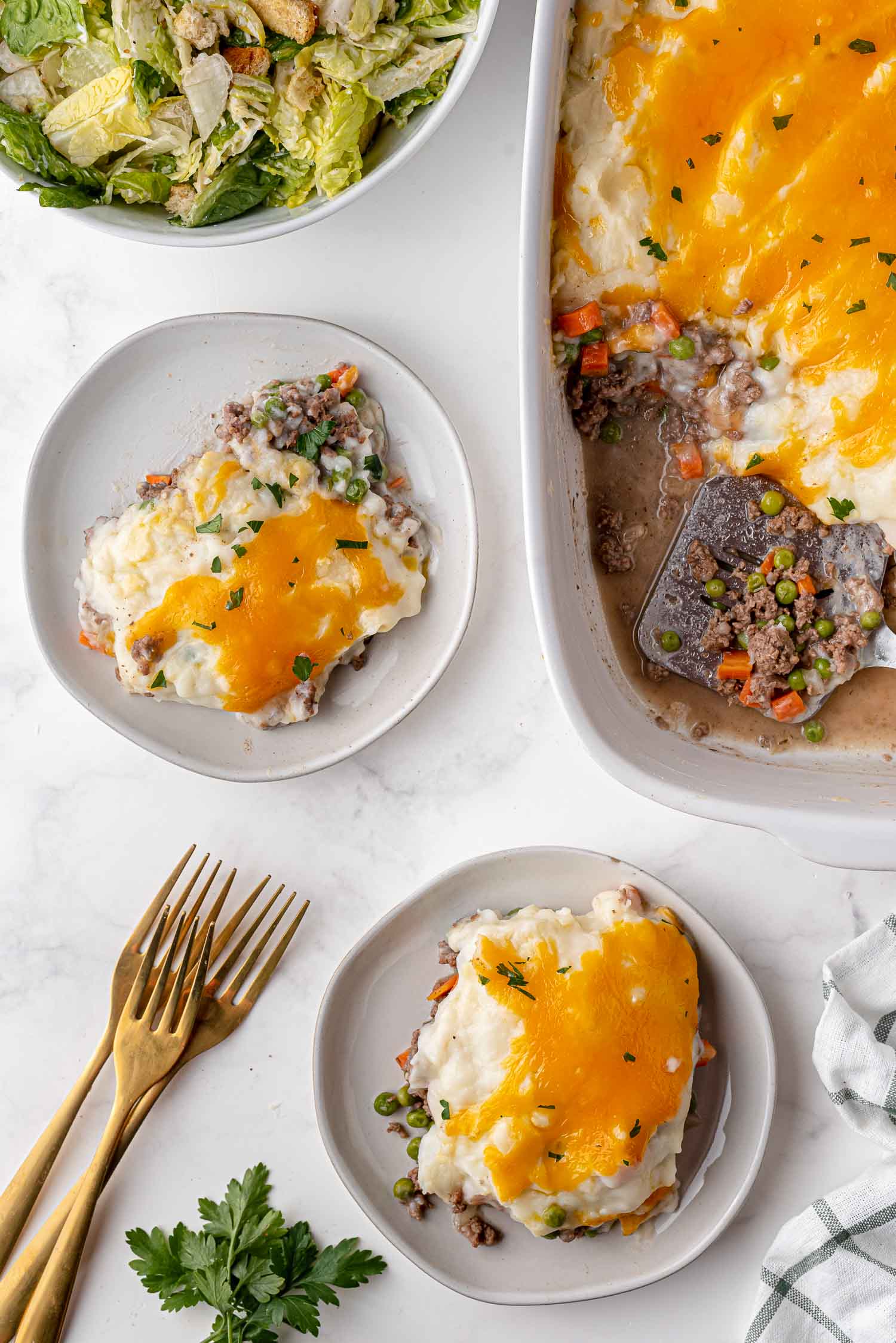 Overhead view of two plates and a casserole dish of shepherd's pie.