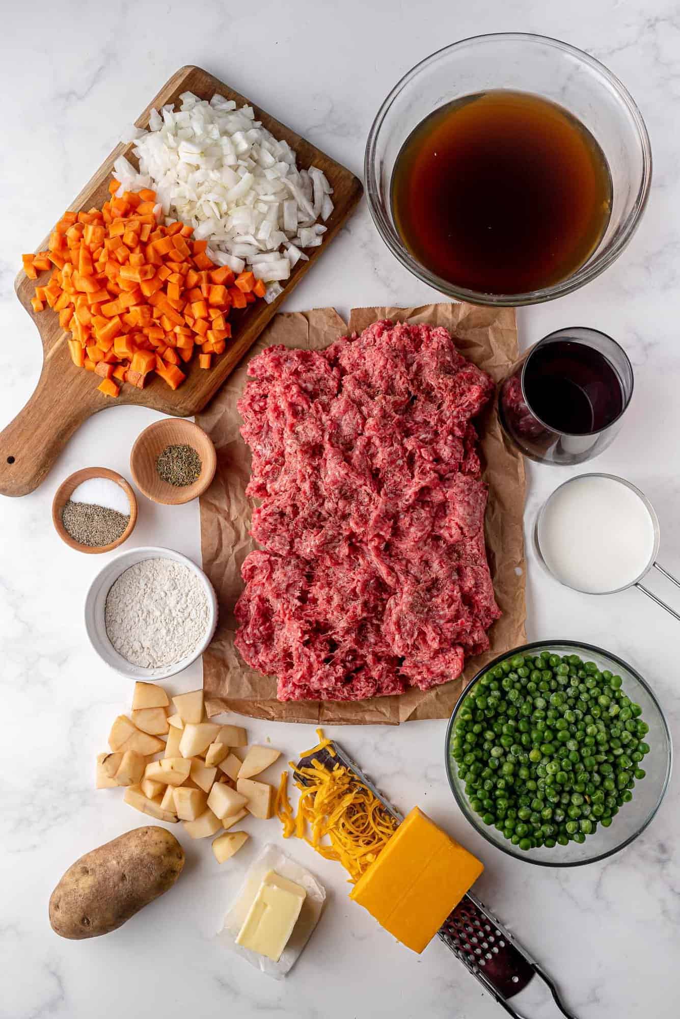 Overhead view of ingredients: Ground meat, vegetables, wine, cheese, potatoes, and seasoning.