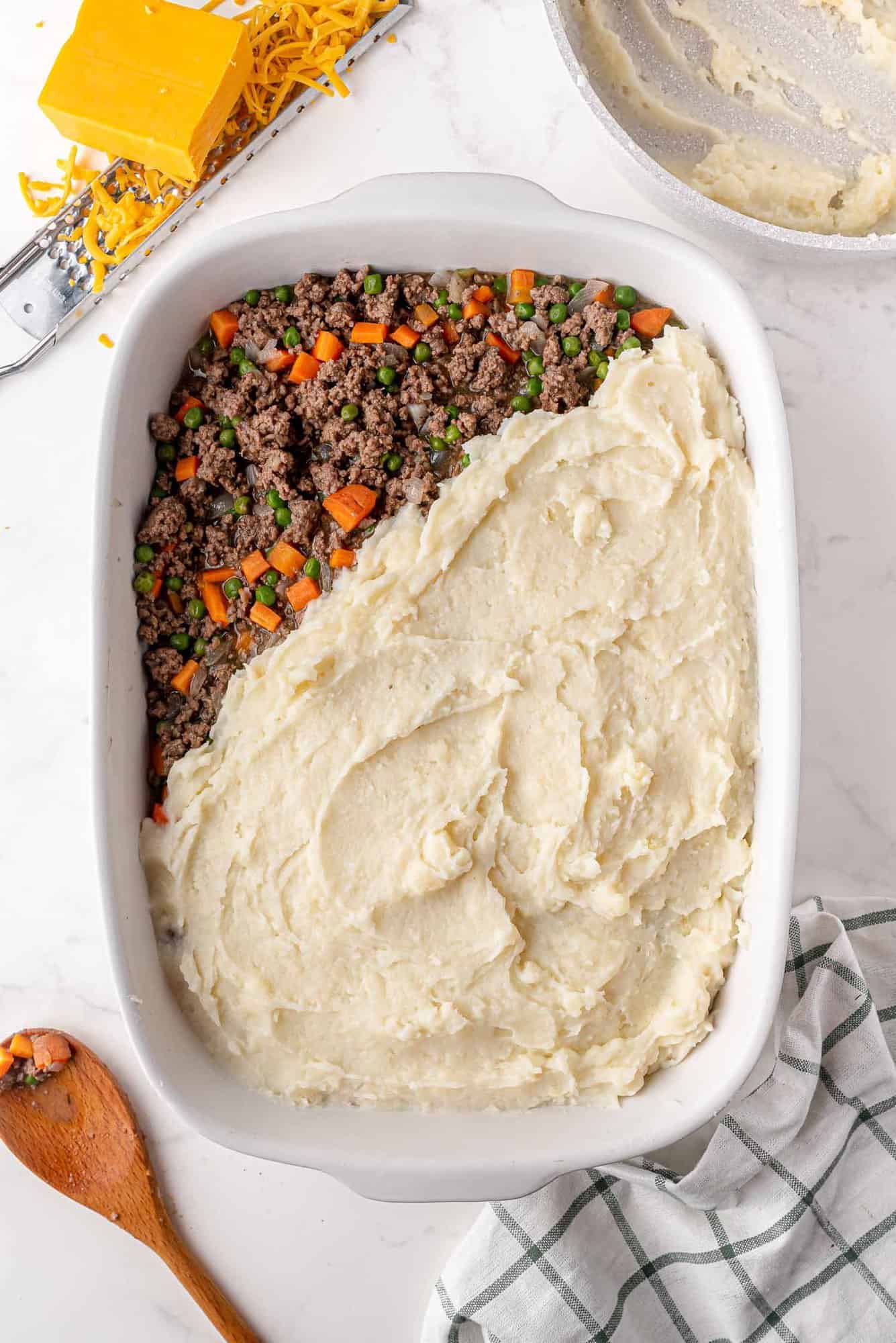 Potatoes being spread on top of ground meat and vegetables in a casserole dish.