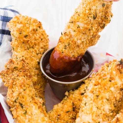 A crispy chicken tender being dipped into bbq sauce.