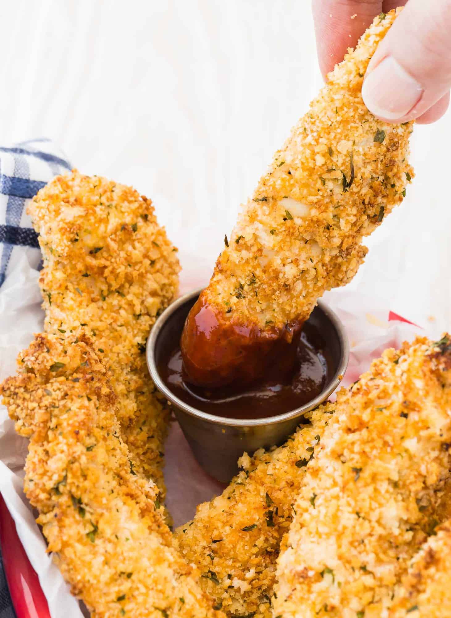 Chicken tenders in a basket, one being dipped in sauce.