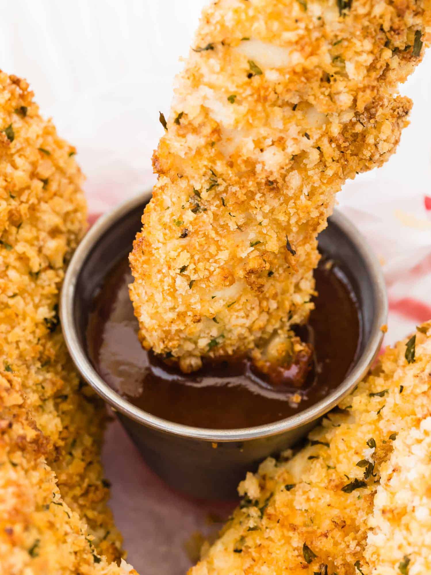 Breaded chicken tender being dipped in barbecue sauce. 