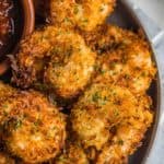 Pile of coconut shrimp on a plate with dipping sauce.