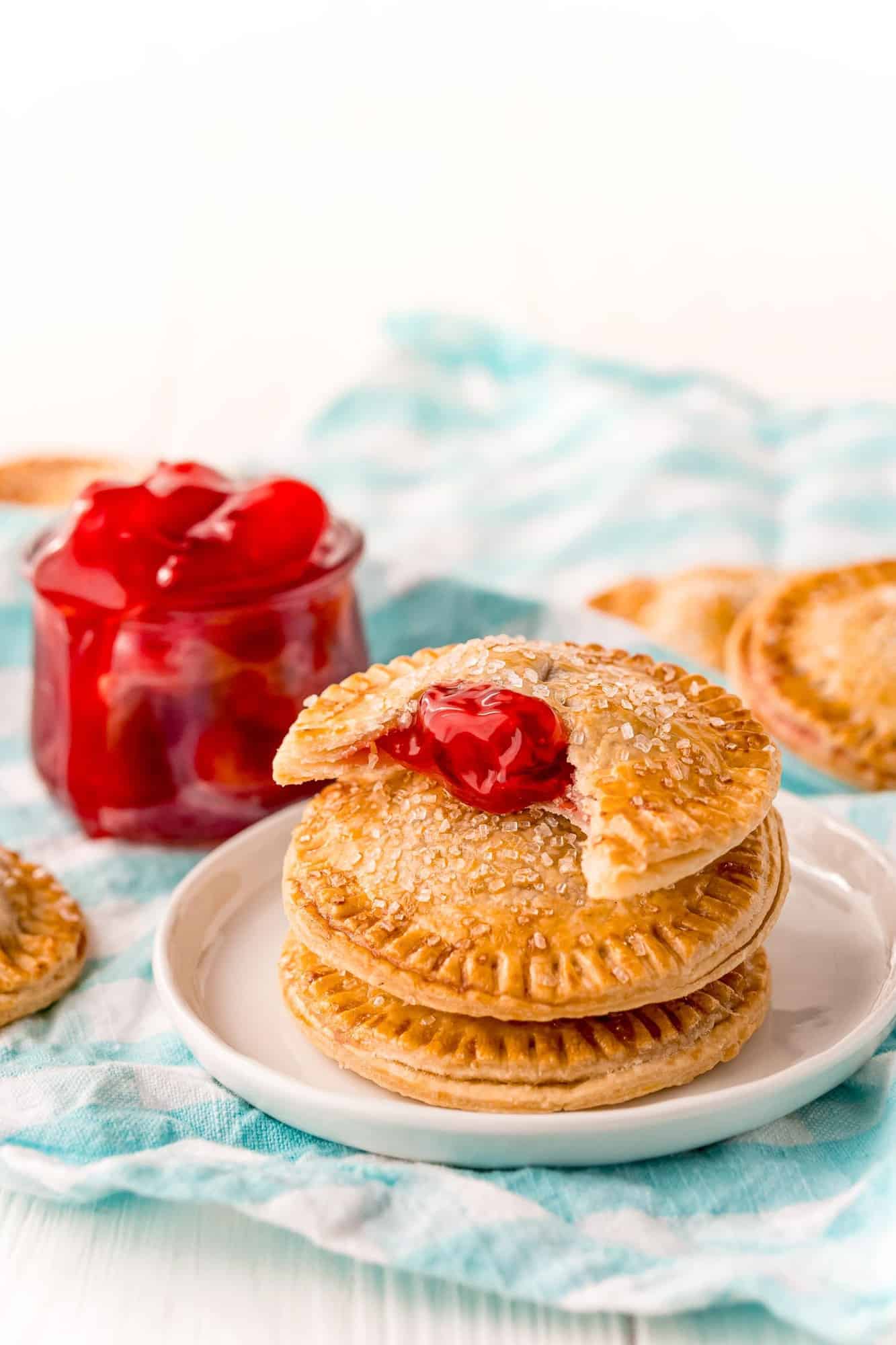 3 hand pies stacked on a plate, one with a bite out of it showing cherry filling.