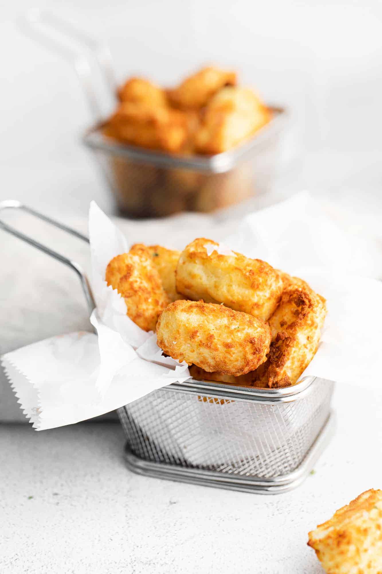 Tater tots in a small metal basket with parchment paper.