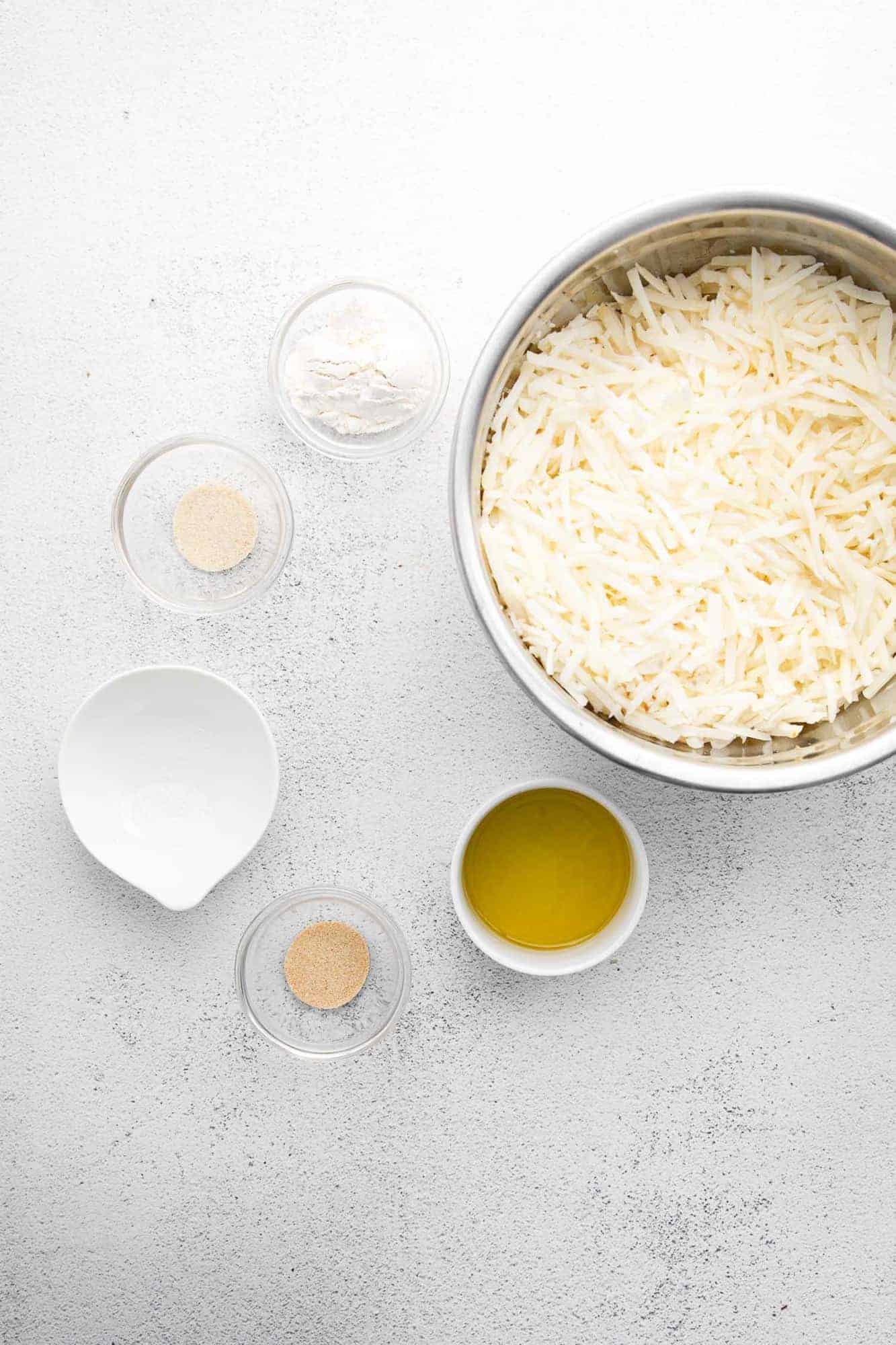 Overhead view of ingredients: shredded potatoes, olive oil, flour, and spices.