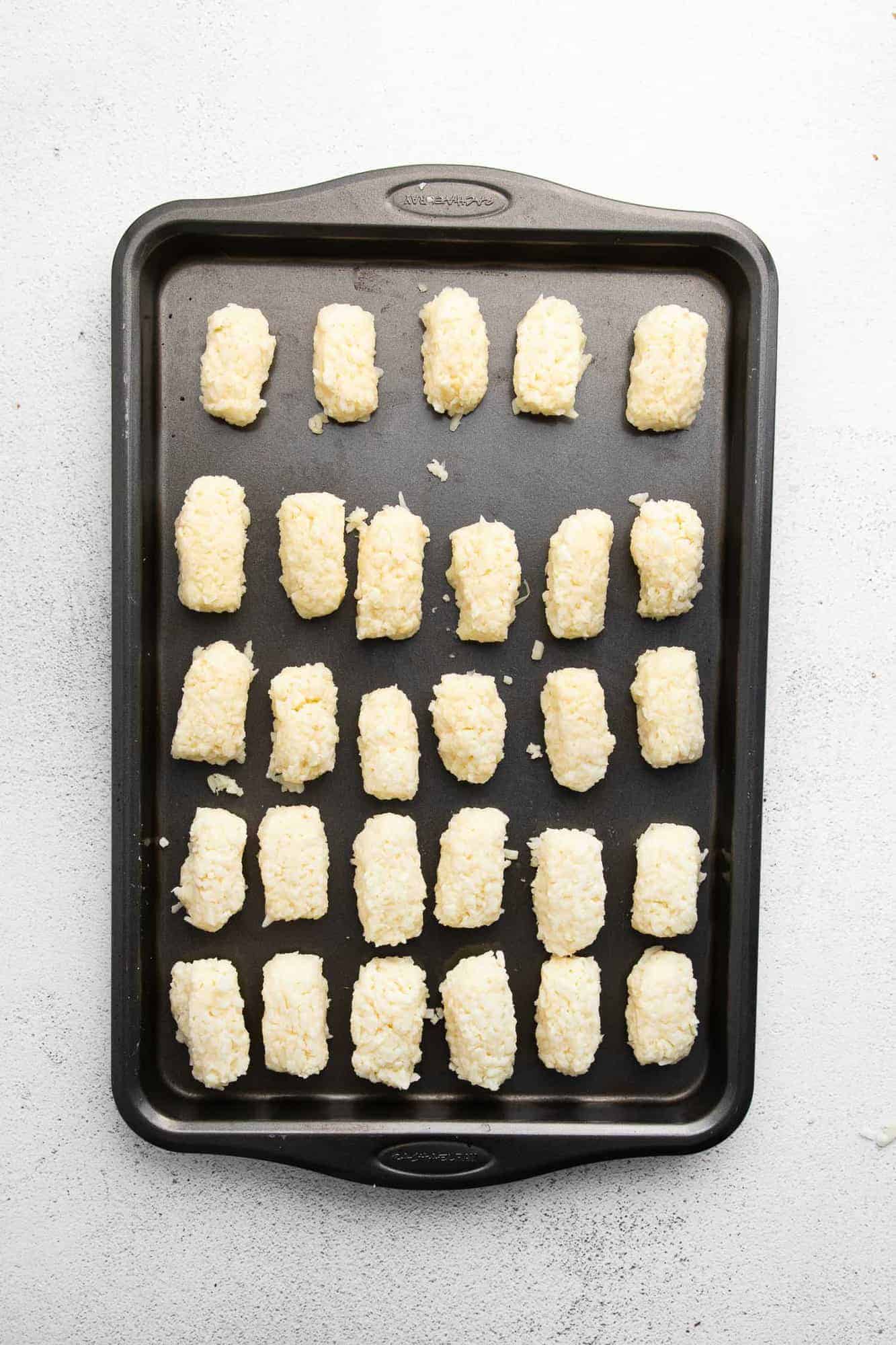 Uncooked homemade tater tots on a baking sheet.