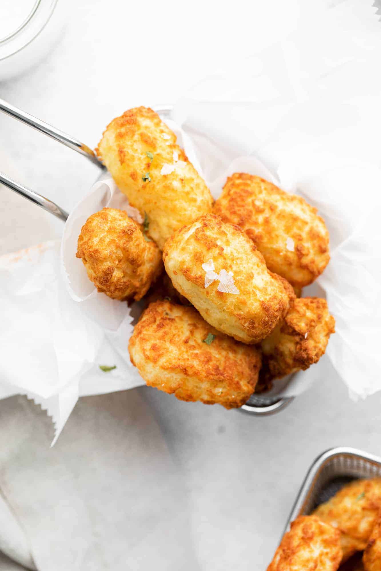 Overhead view of tater tots in a small metal basket on a white background. 