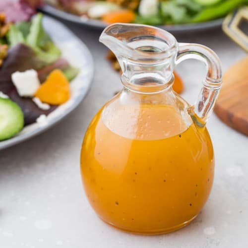 Bright orange salad dressing in a jar in front of salads.