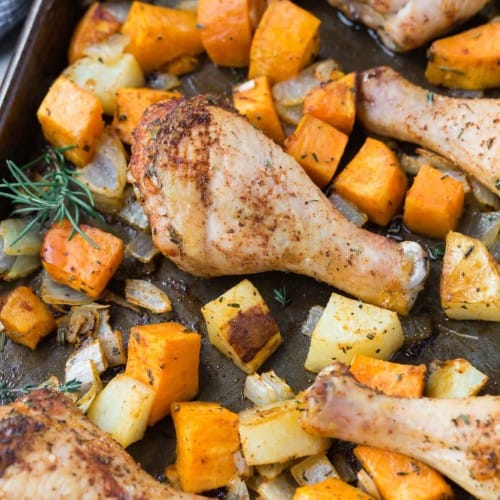 Chicken drumsticks and cubed potatoes and sweet potatoes on a sheet pan.