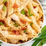 Pasta with chicken, cheese sauce, bacon, and green onions, in a white bowl.