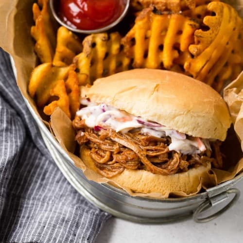 Instant Pot Pulled Pork on a bun with slaw and fries in a basket.