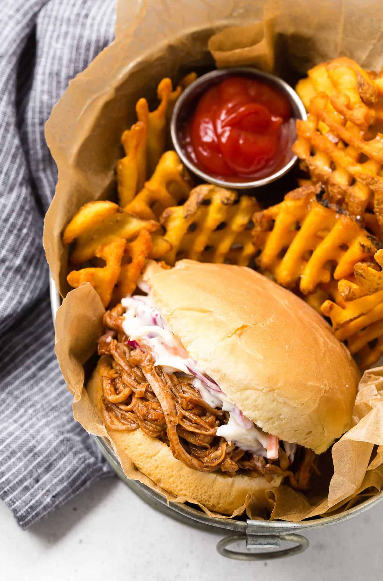 Pulled pork sandwich in a basket with waffle fries.