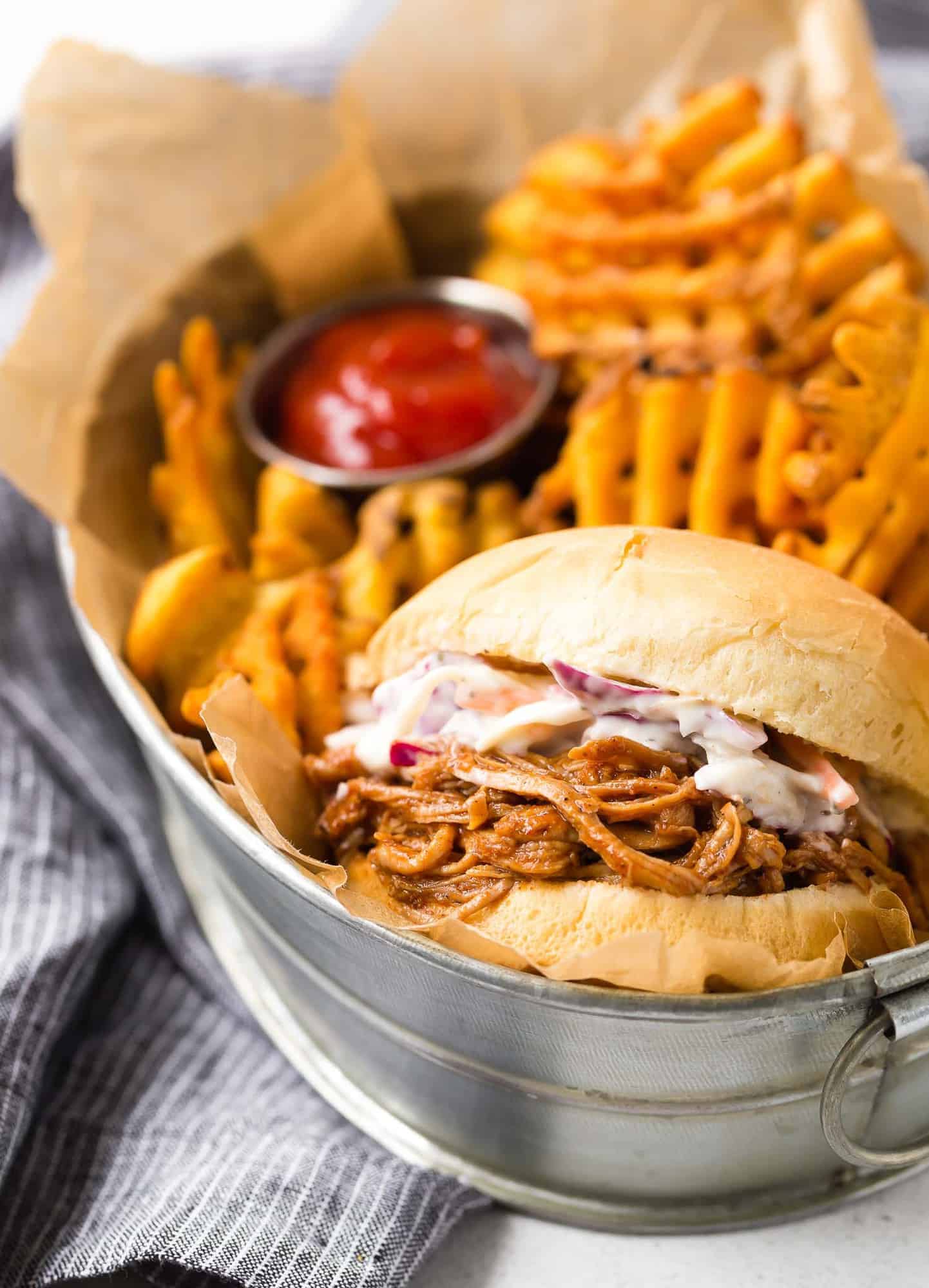 Sandwich with pulled pork and coleslaw in a basket with fries.