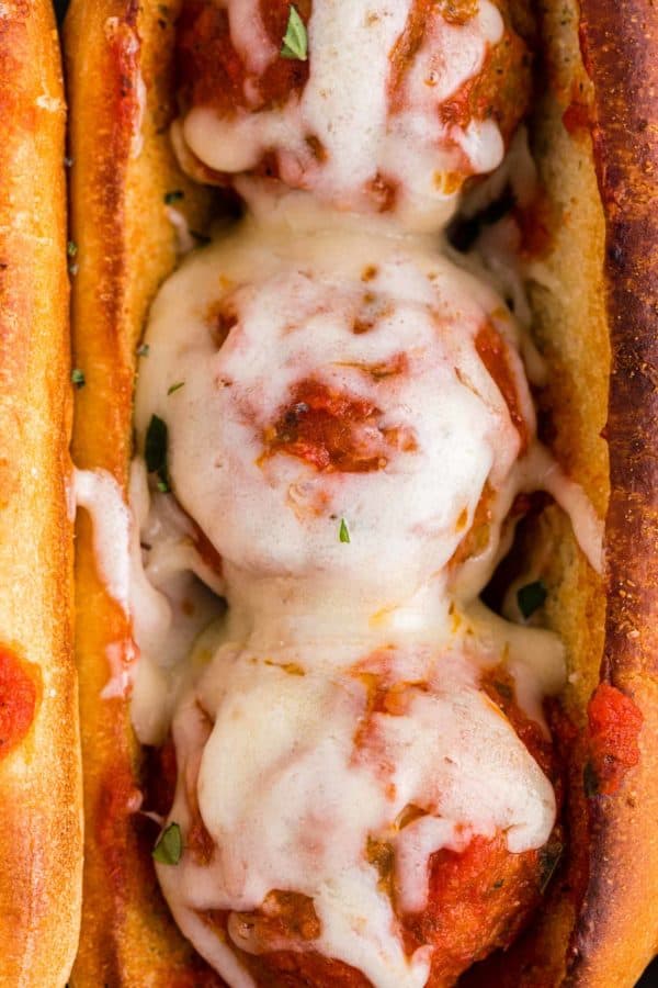 Close up of a sauce and cheese covered meatball on a sub bun.