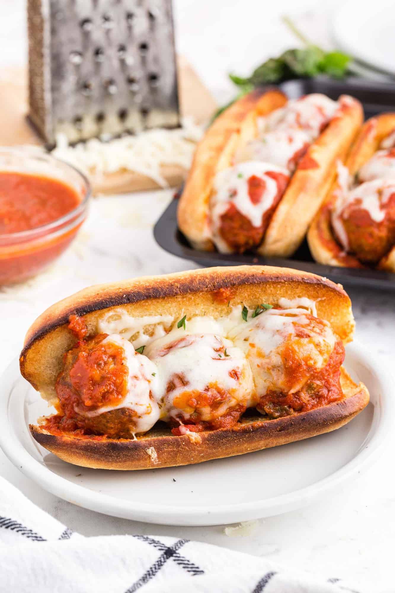 Meatball sub on a white plate with more sandwiches in the background.