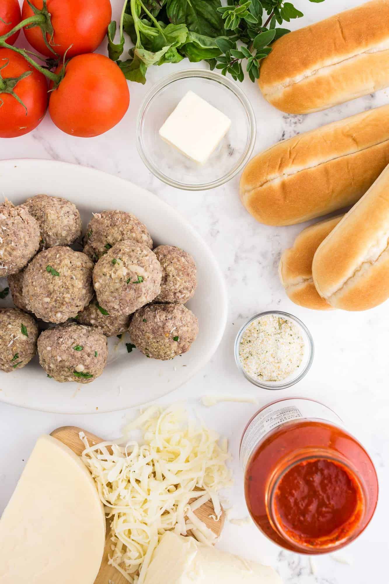 Overhead view of ingredients including sub buns, meatballs, tomato sauce, cheese.