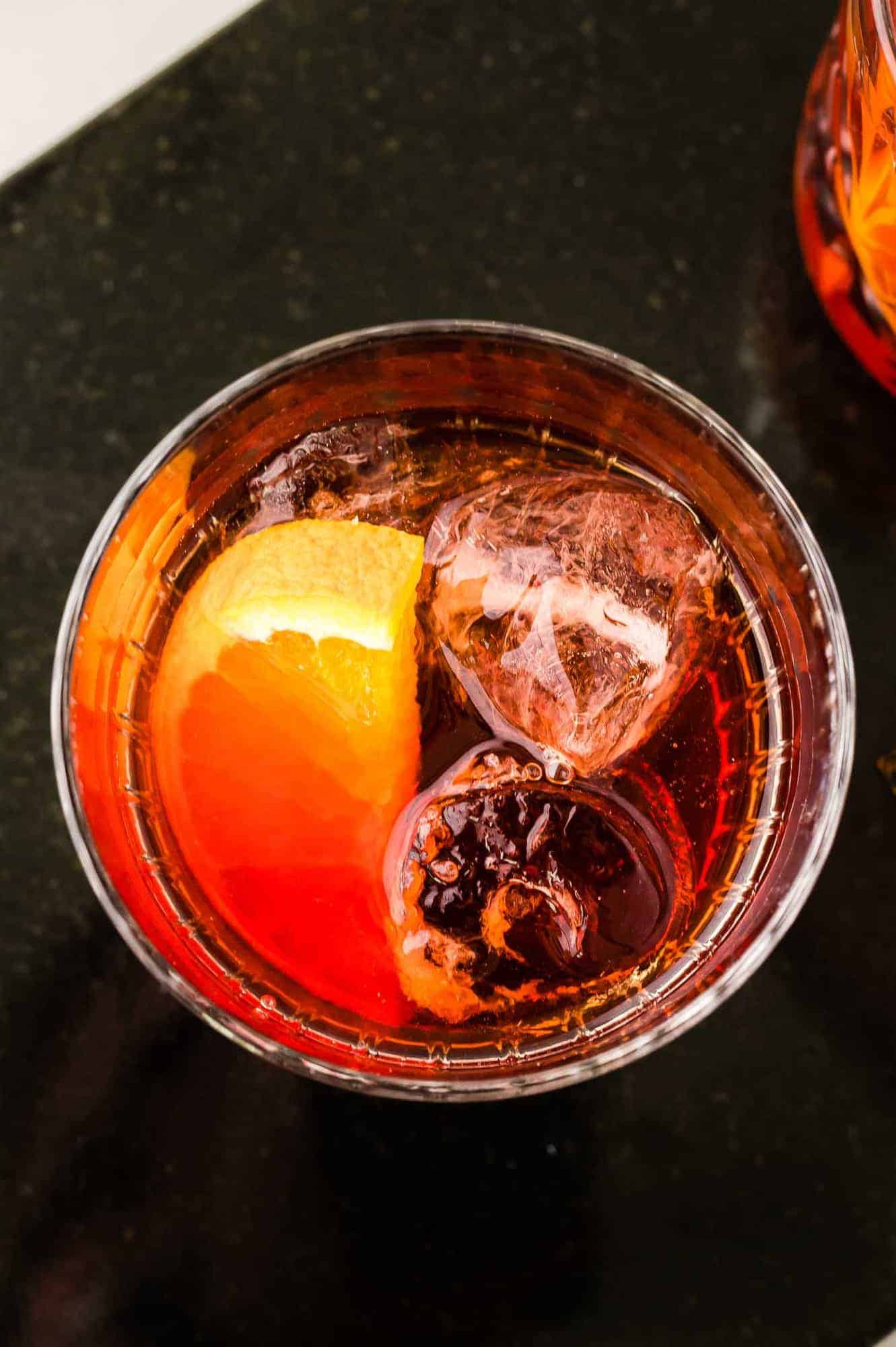 Overhead view of a drink with ice and an orange slice, on a black background.