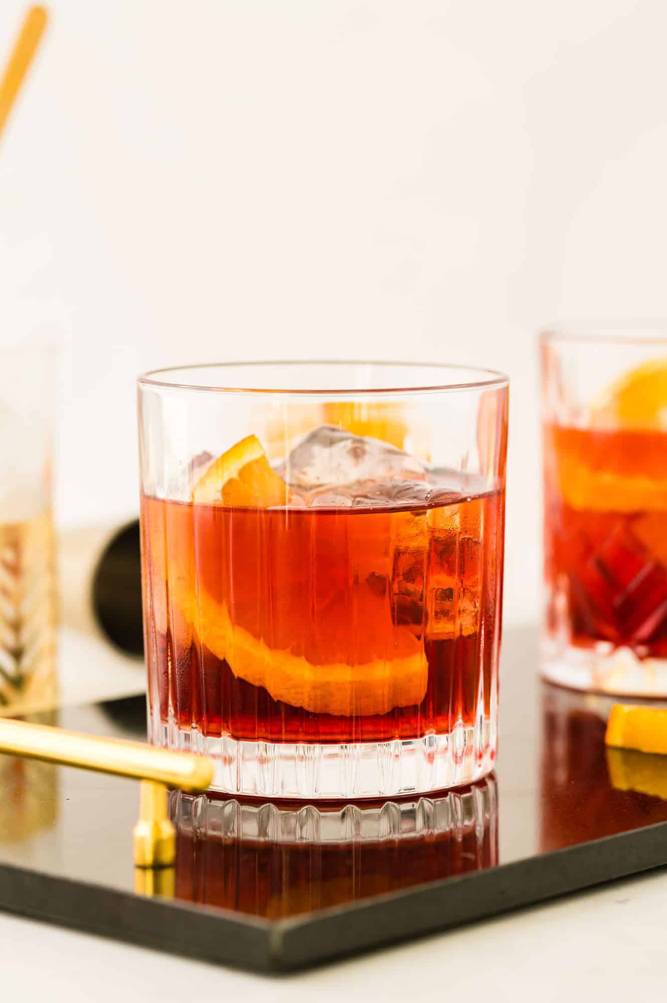 Dark red beverage in a short glass, with ice and an orange slice.