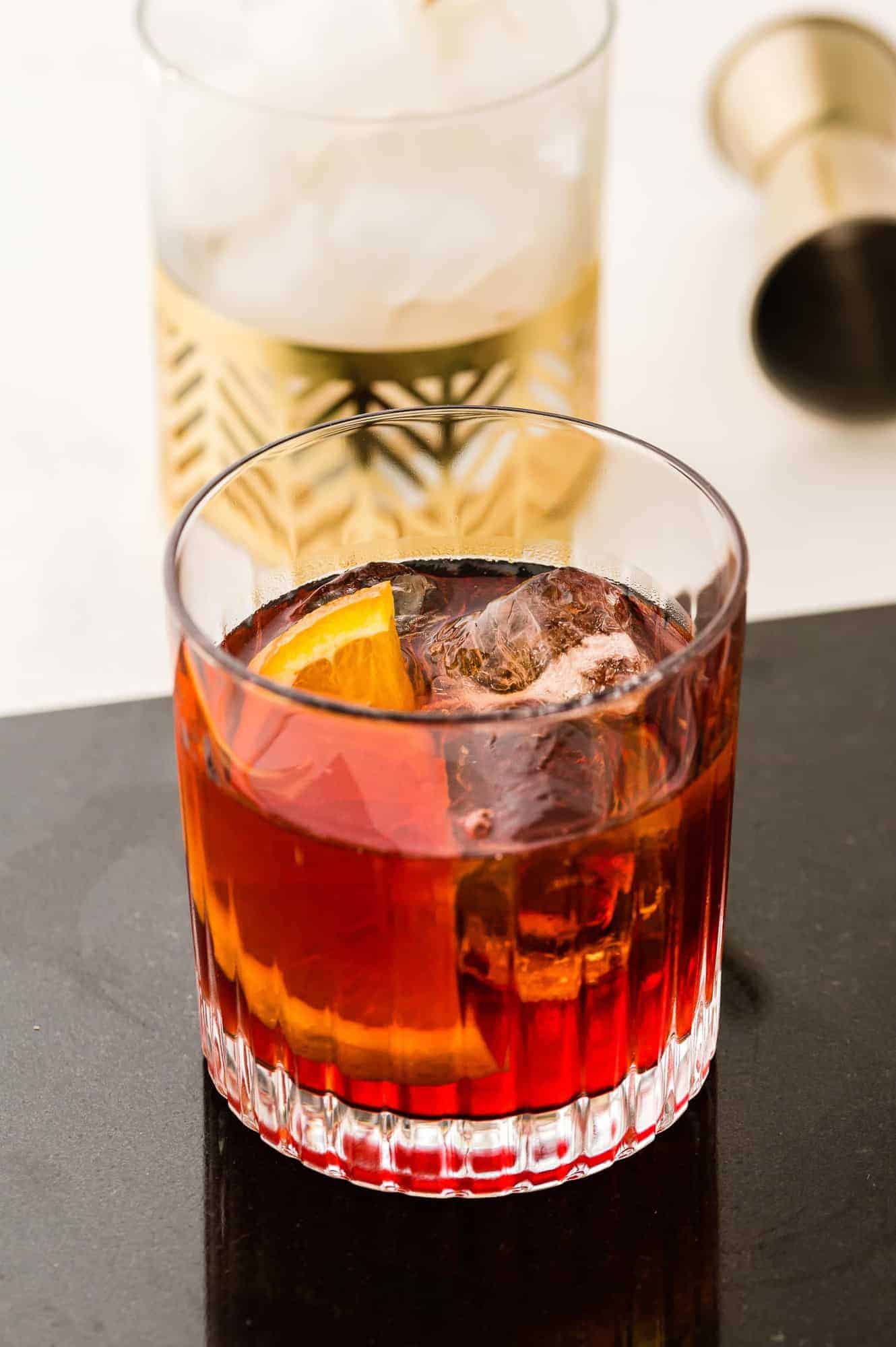 Dark red cocktail over ice, on a black tray.