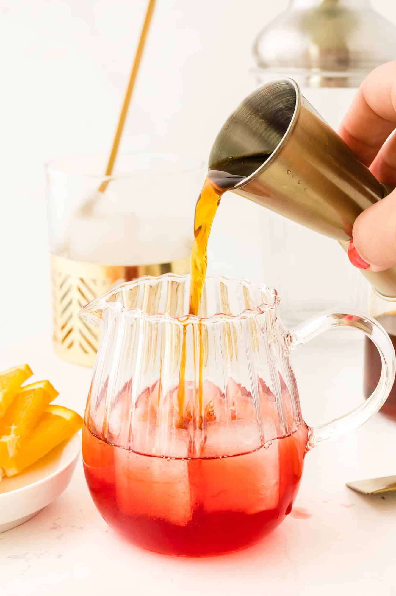 Liquid being poured from a jigger into a glass mug.