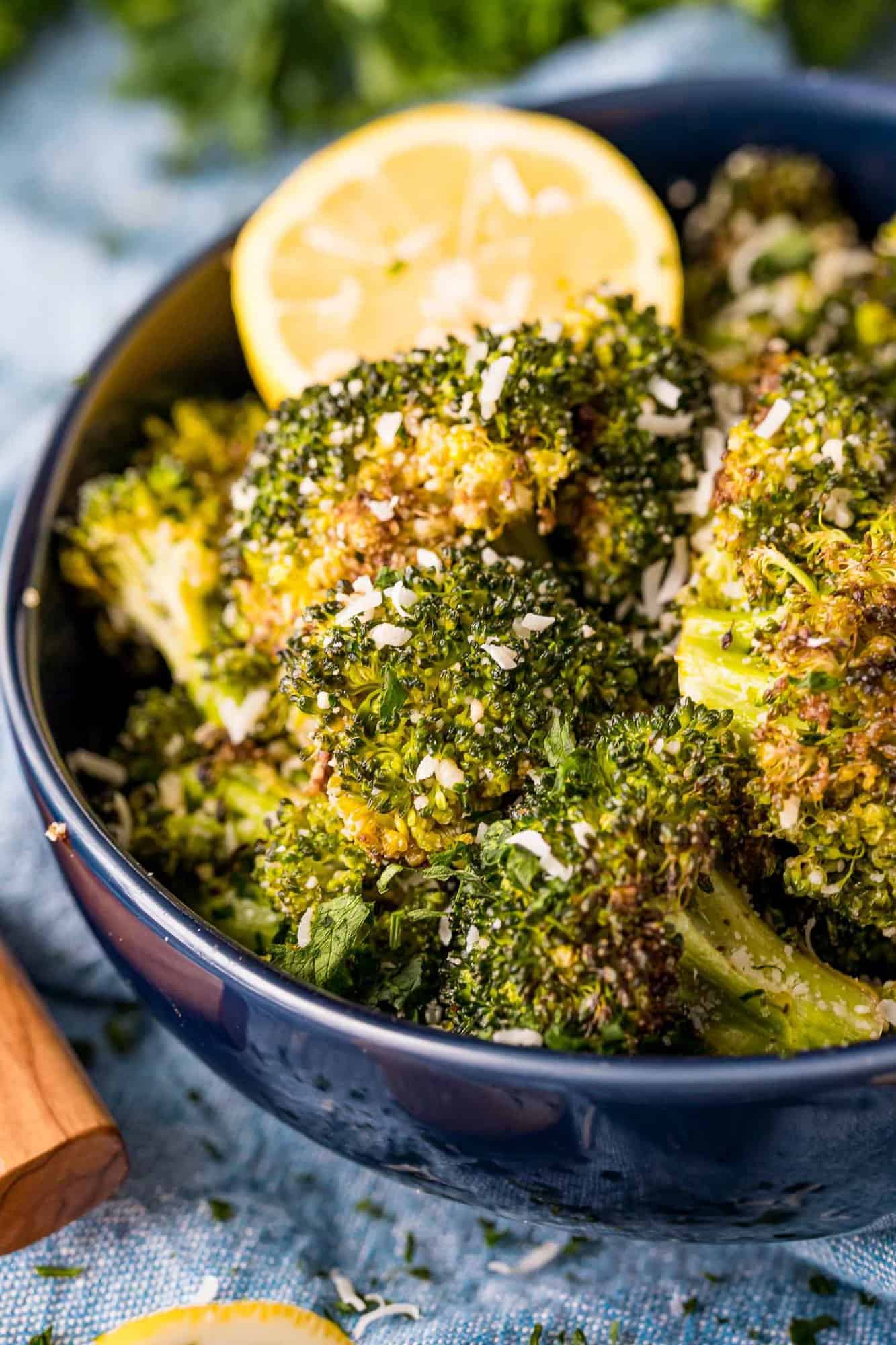 Broccoli roasted with lemon and parmesan in a bowl with lemon slice.
