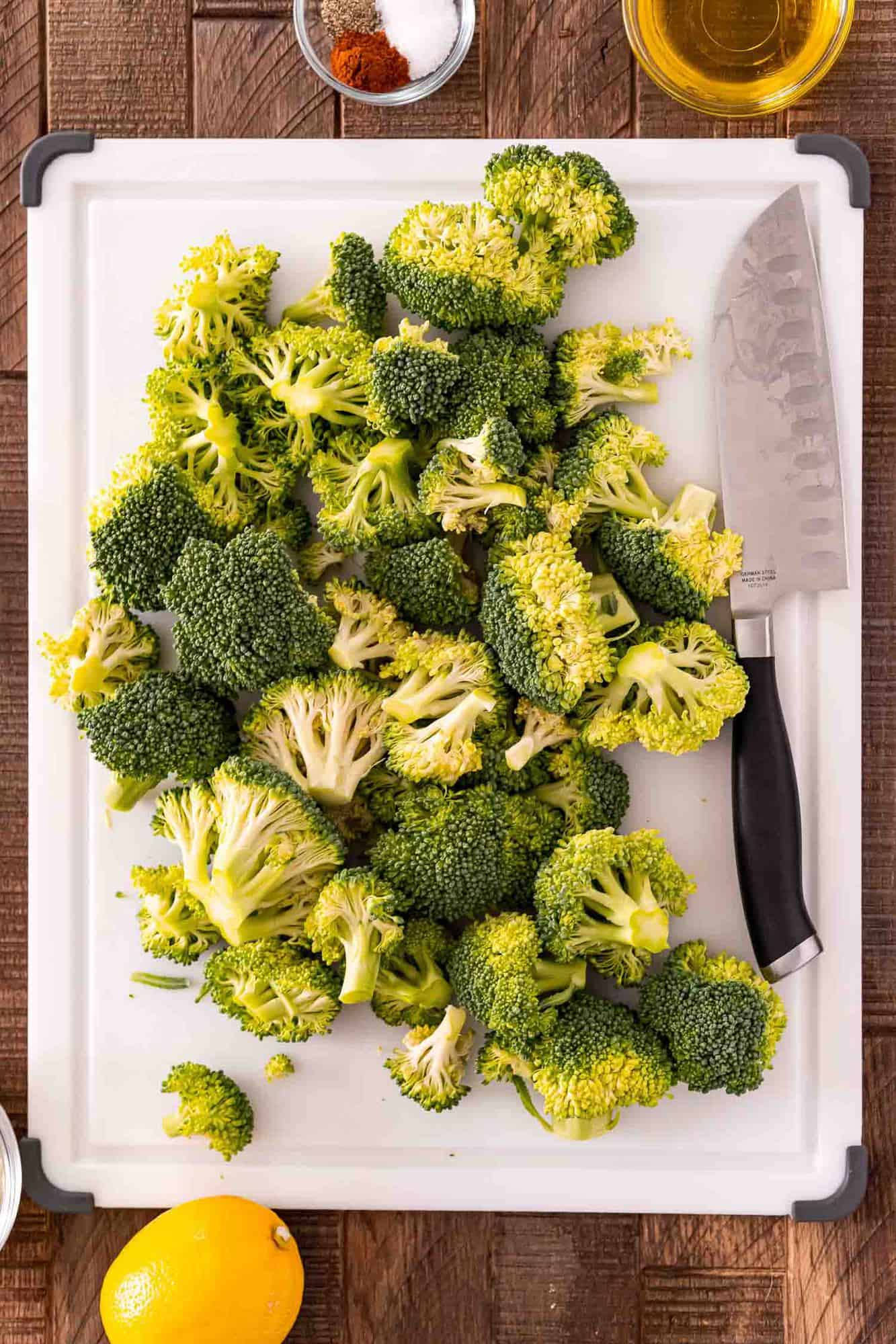 Broccoli florets and knife on white cutting board.