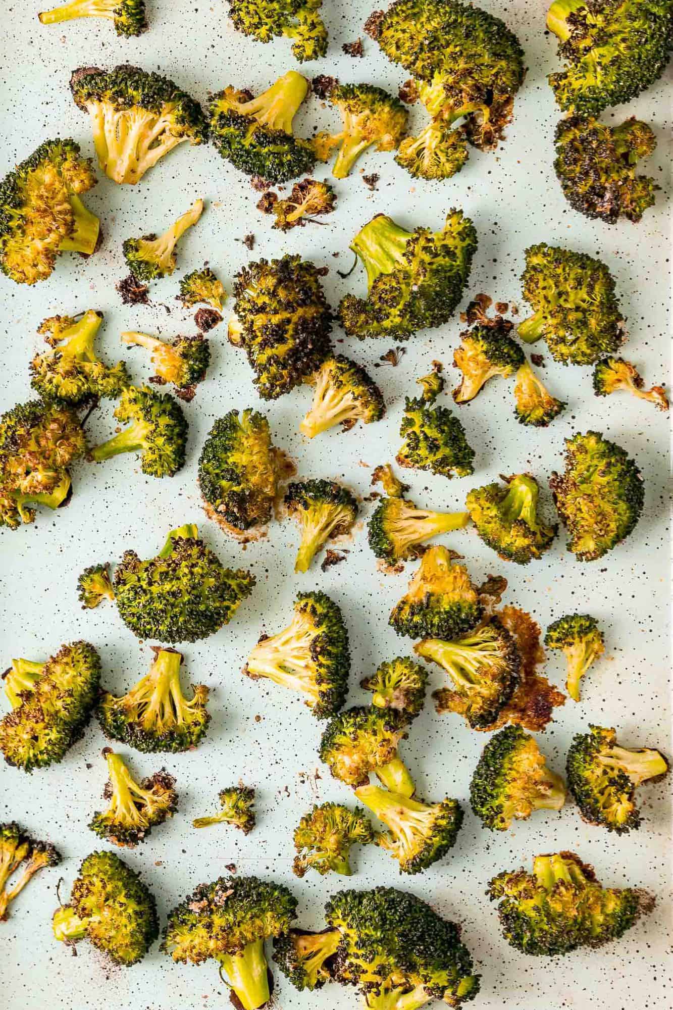 Roasted broccoli on a parchment paper lined sheet pan.