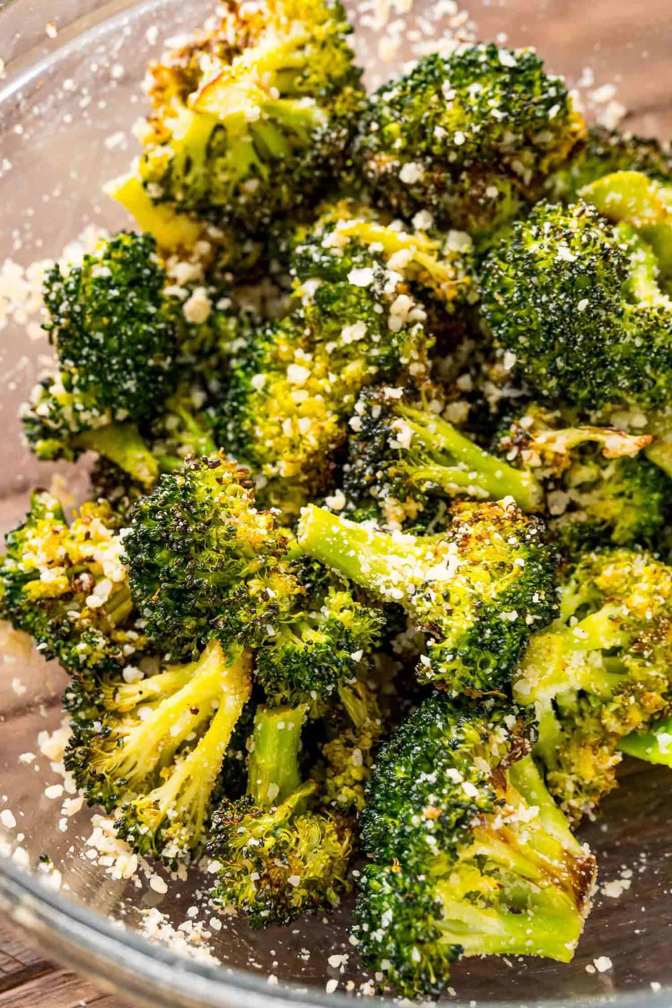 Roasted broccoli in a bowl being tossed with Parmesan.