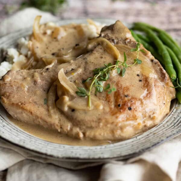 Pork on a plate with mushroom gravy, topped with fresh thyme.
