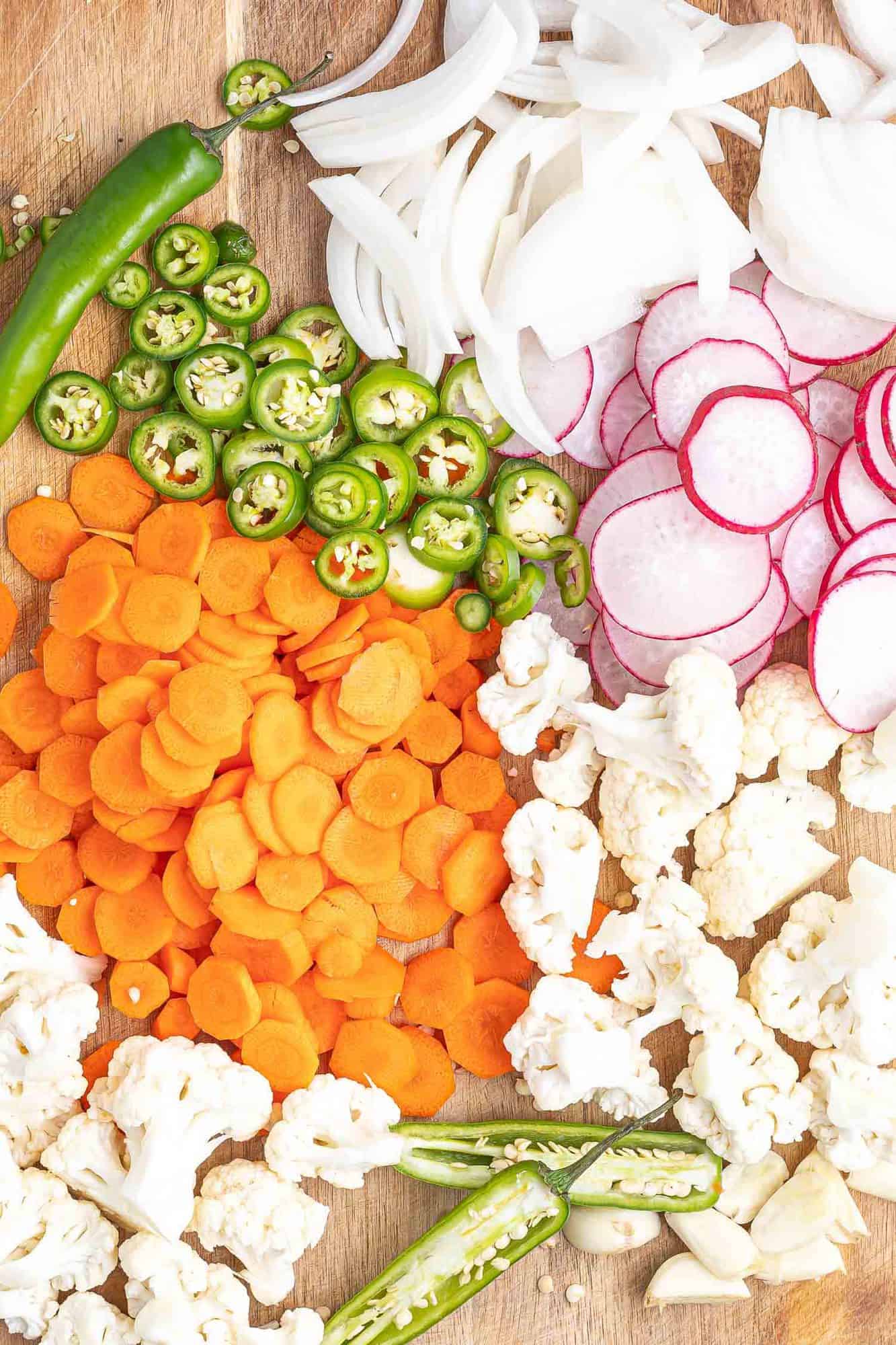 Assorted cut vegetables on a wooden surface: radishes, jalapeno, carrots, cauliflower, and onion.