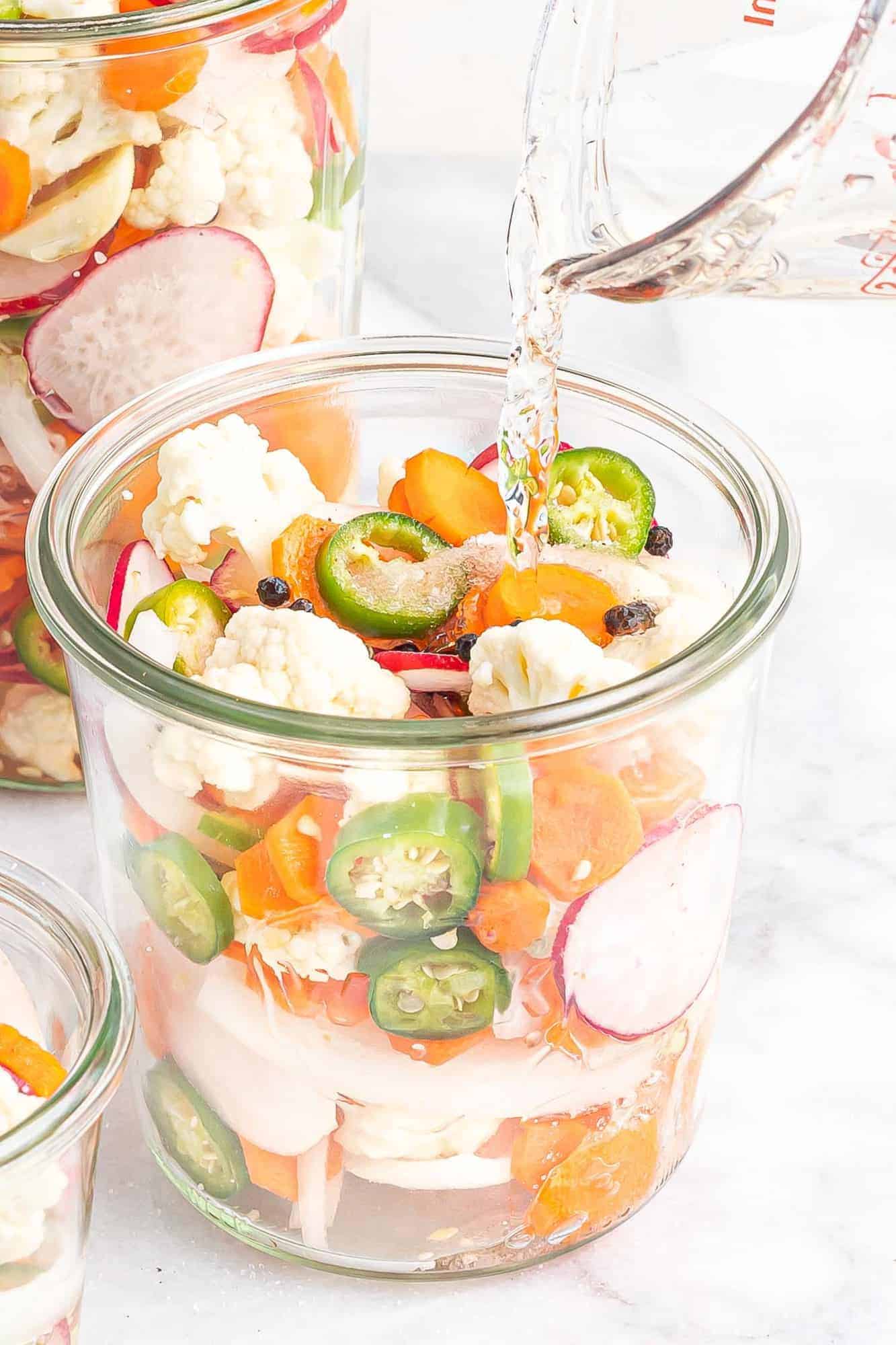 Liquid being poured into a jar of cut vegetables.