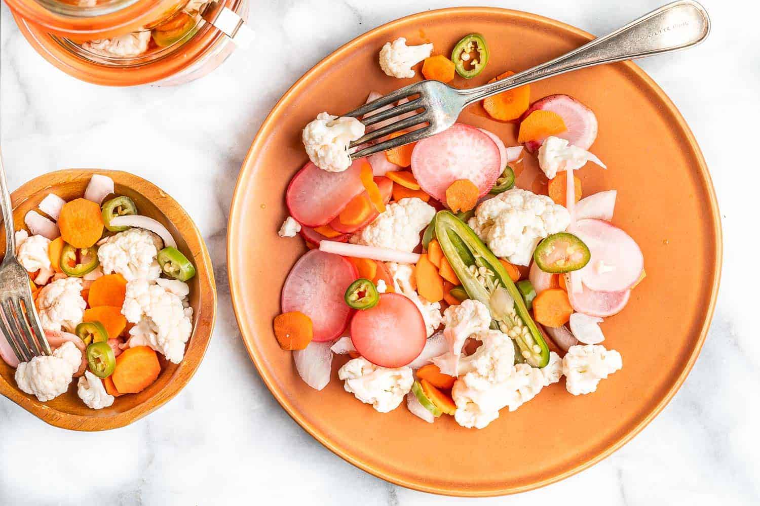 Mixed vegetables that have been pickled, on an orange colored plate.