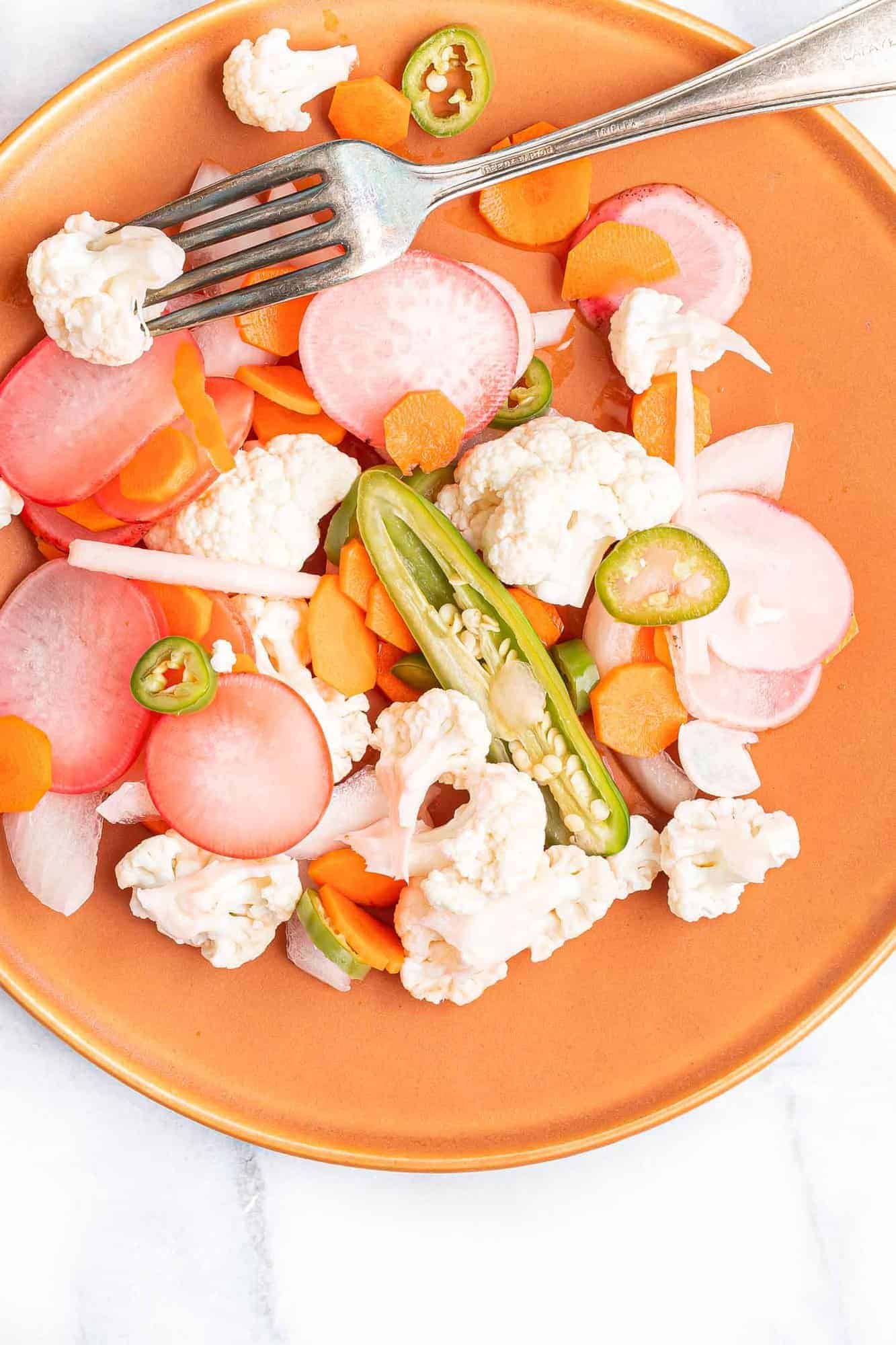 Pickled vegetables on a reddish orange plate.